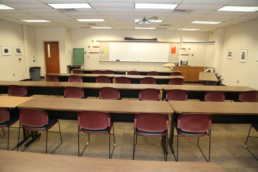 Flexible classroom with long tables and 2 chairs per table, white board and screen