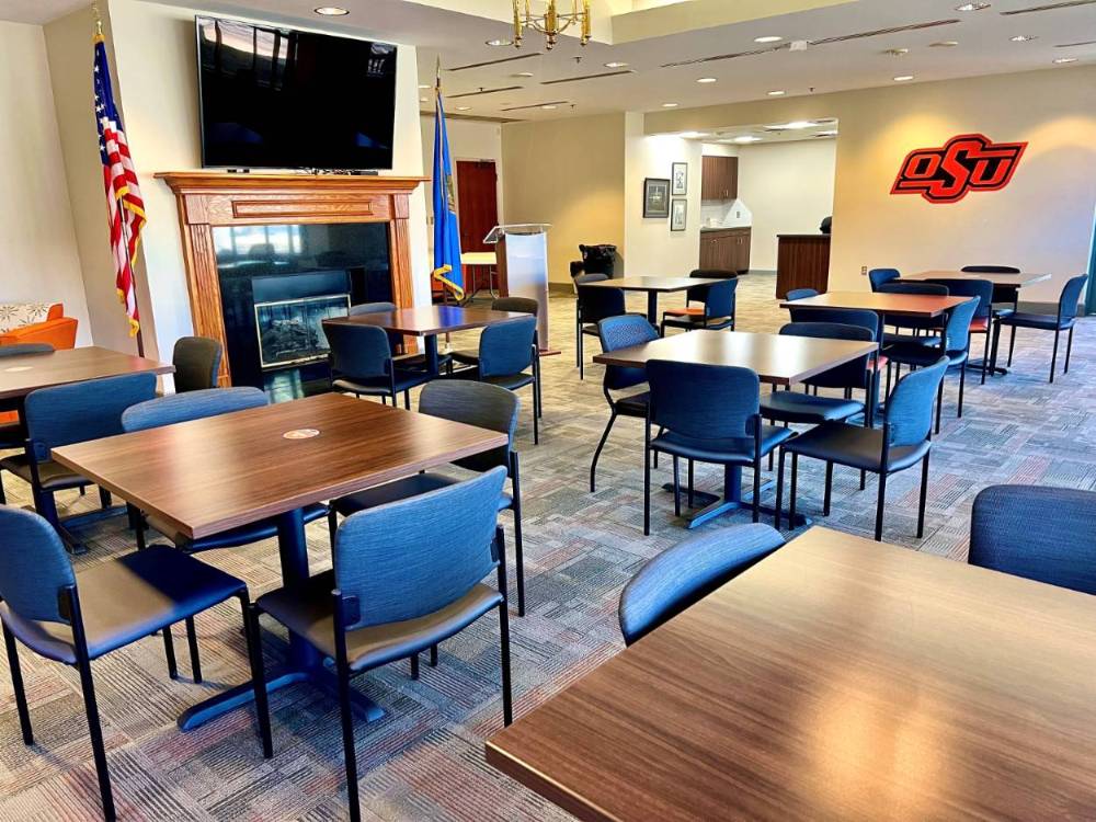 Tulsa room set up with empty square tables and four chairs per table, with a smart tv on the wall.