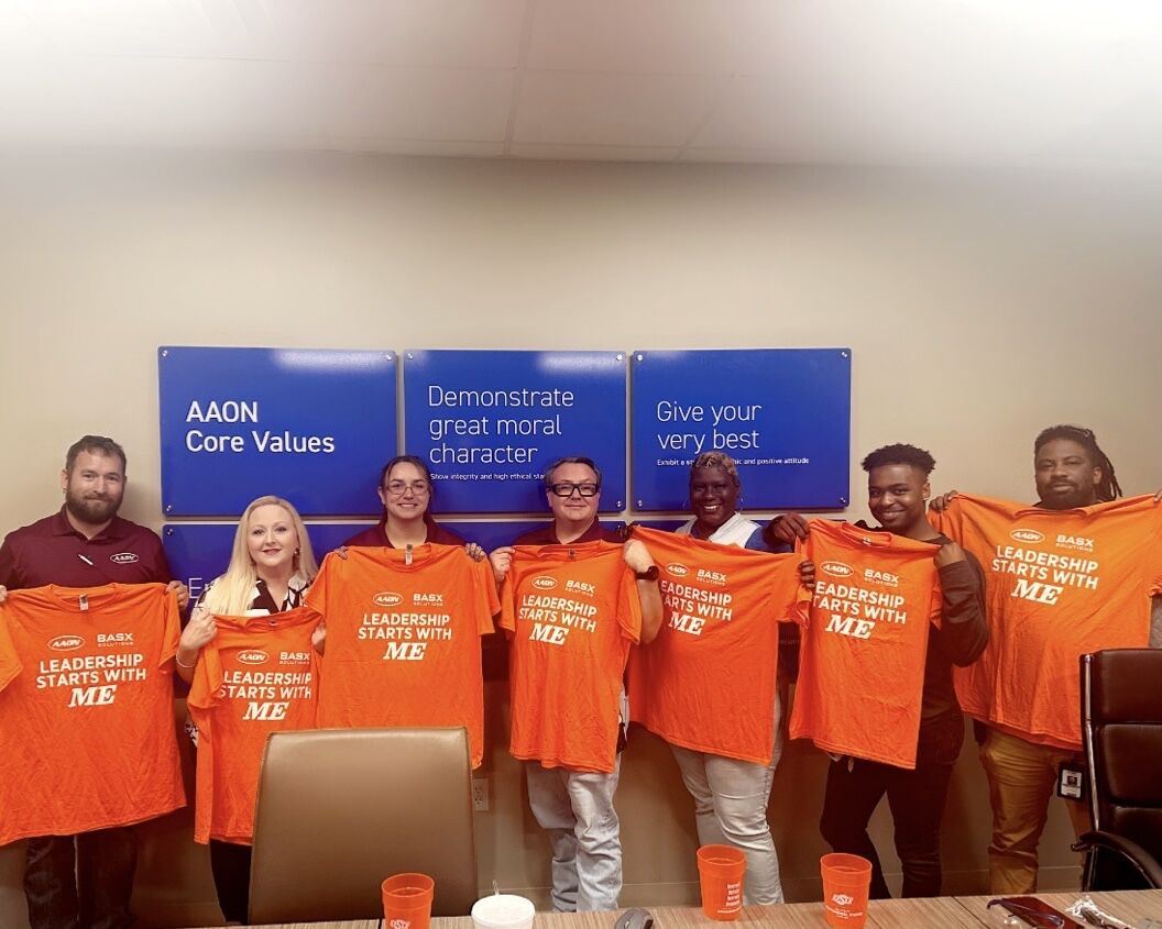 A group of AAON employees stand in a line holding up orange t-shirts that read "Leadership starts with me"
