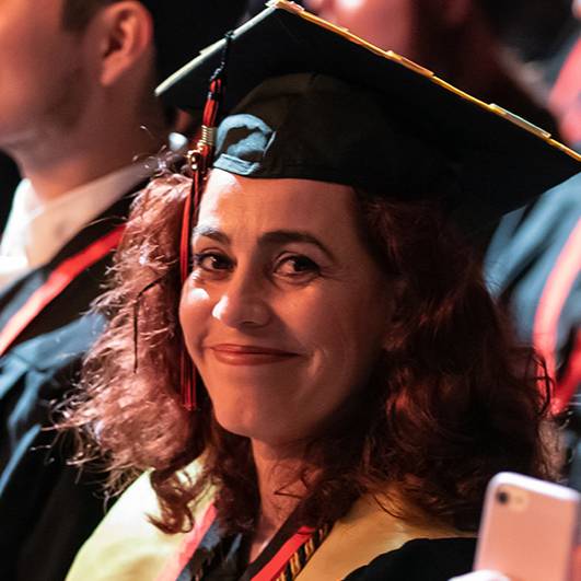 Woman wearing graduation regalia and smiling at the camera