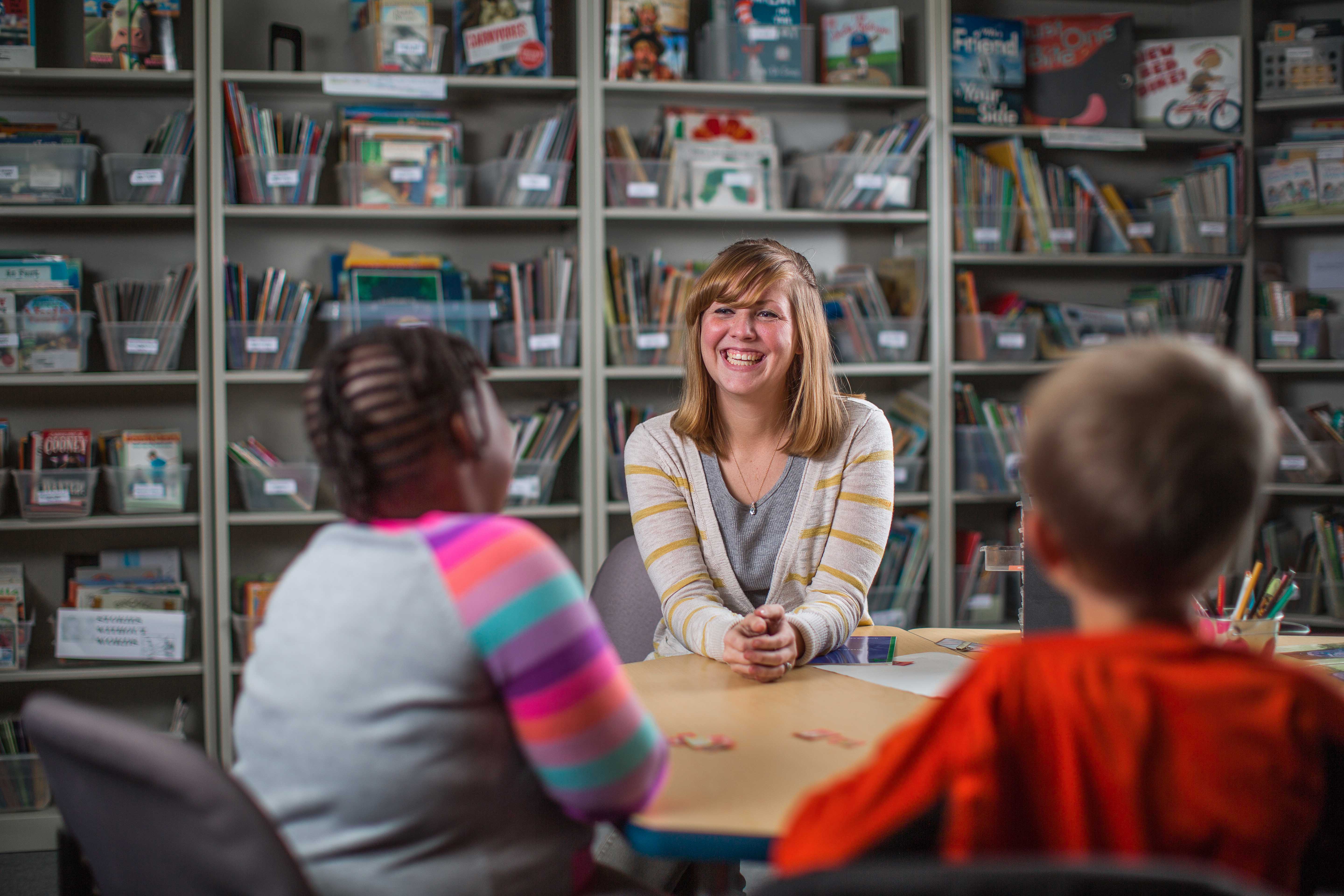 woman smiles, seated across the table from two children