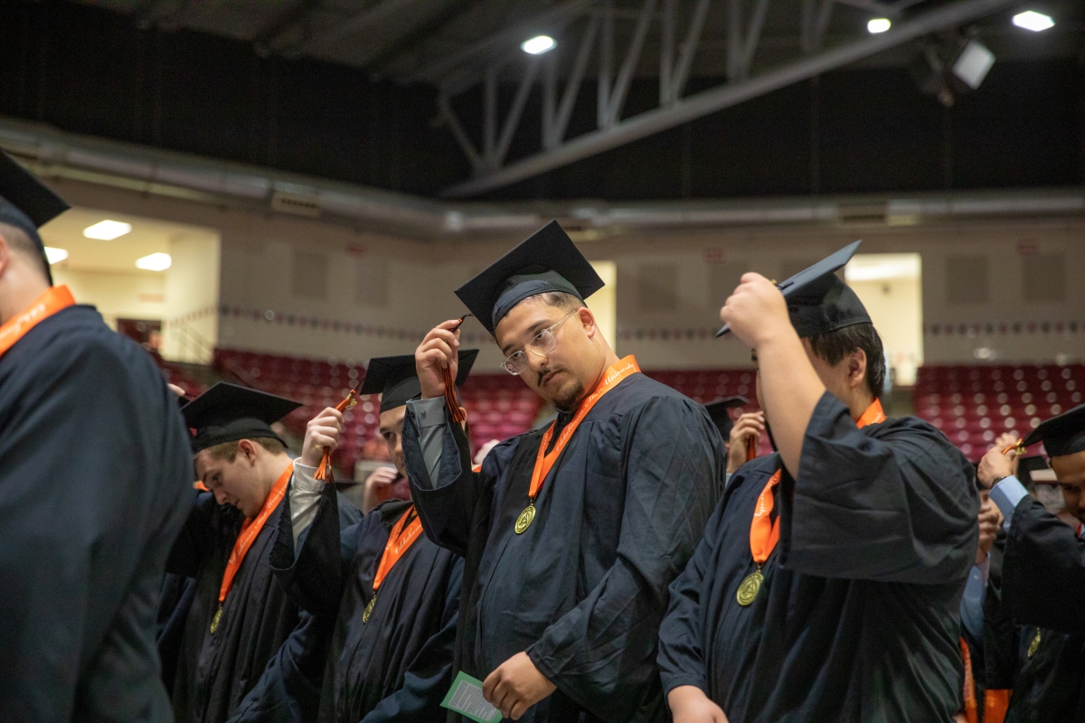 Graduates hold their tassels to move them over during graduation ceremony