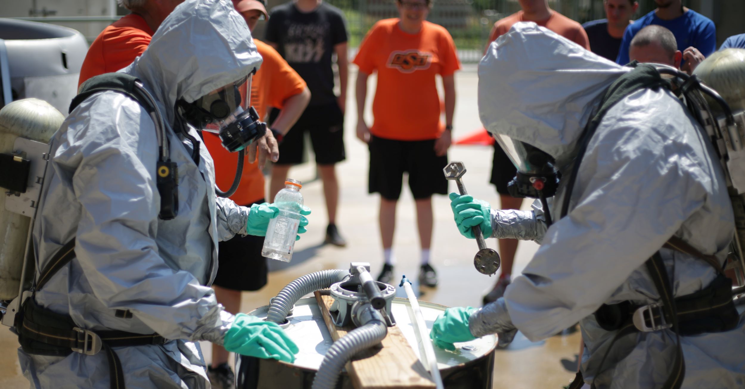 Two people wearing HAZMAT suits work on a simulation.