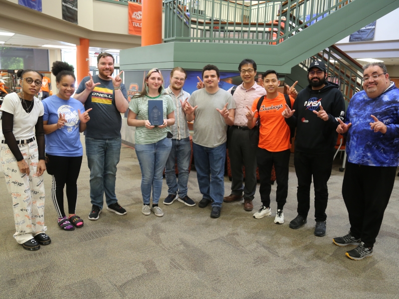MIS Club members stand in the lobby of North Hall making the Go Pokes gesture with their handsand gather award their award.