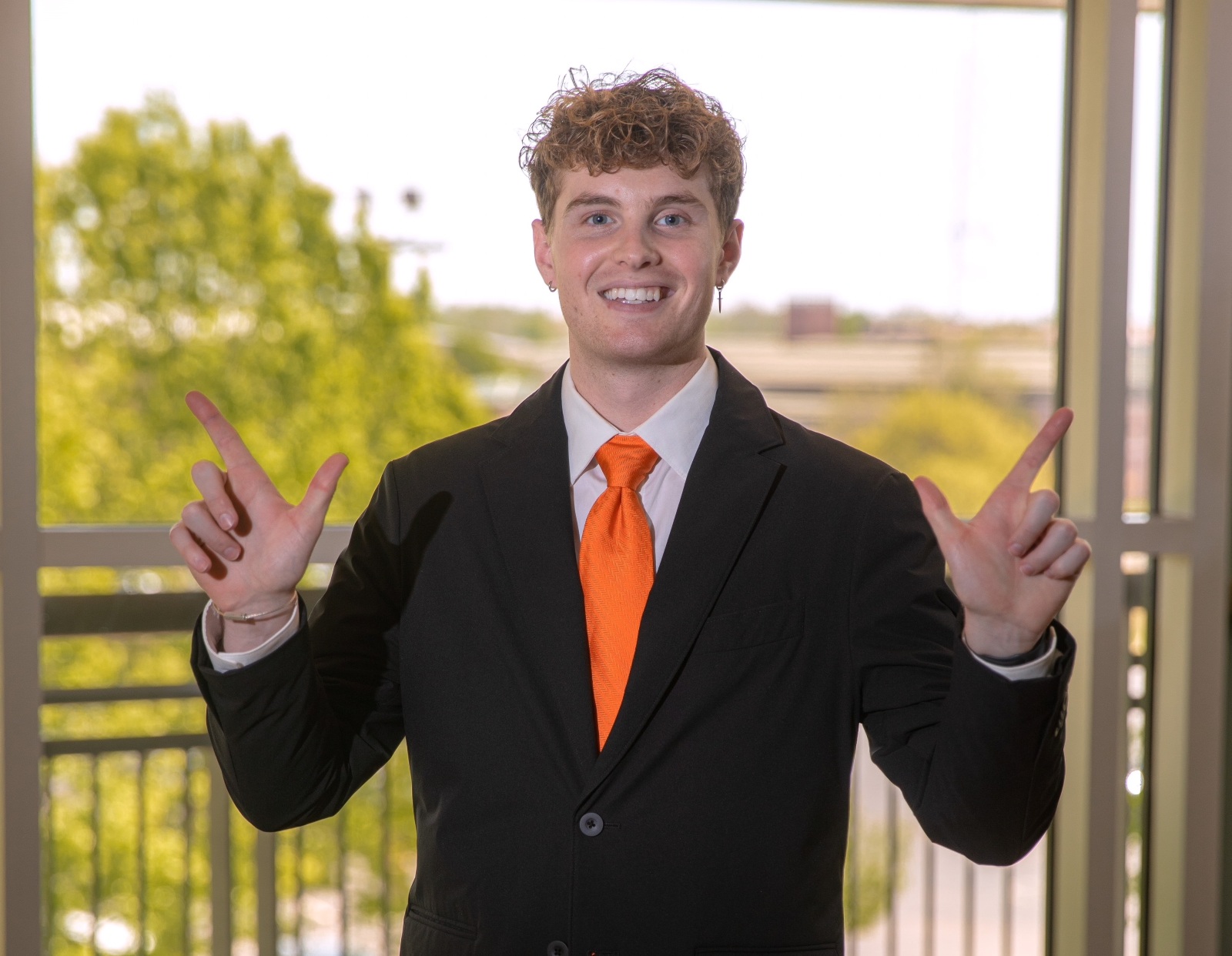 student Lane King stands in front of window doing the "go pokes" sign